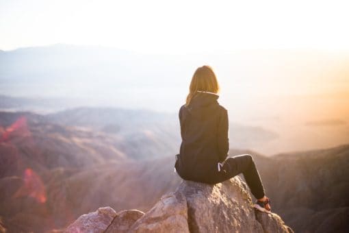 Woman sits on a mountaintop in pursuit of Christian joy