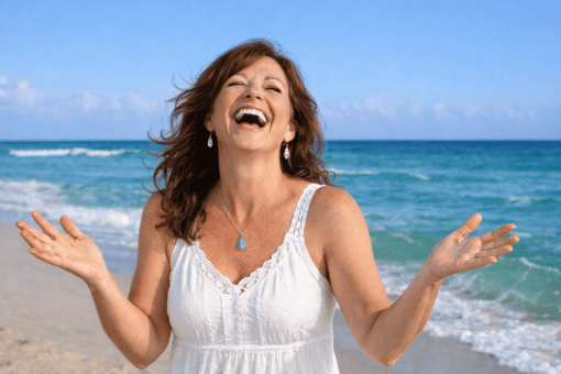 Woman in white dress laughs and enjoys her calling and purpose on a beach with head back and arms out